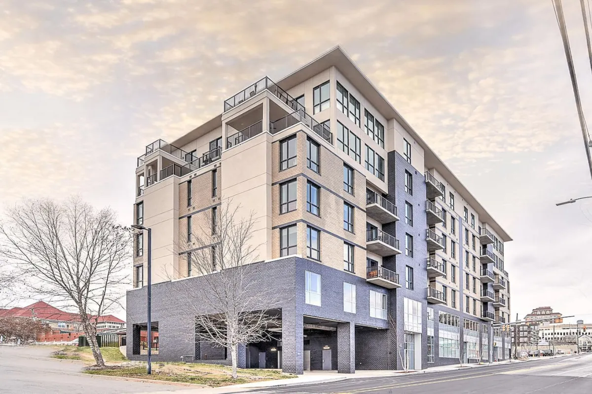 The exterior of a modern building, showcasing multiple balconies, large windows, and ground-level commercial space. The atmosphere is lively and contemporary, capturing the energy of city living.