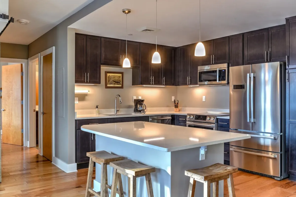 A high-end kitchen scene with a spacious island, sleek stainless steel appliances, dark cabinetry, and pendant lighting. The arrangement encourages socializing and meal preparation, with plenty of space for cooking or enjoying coffee with companions.