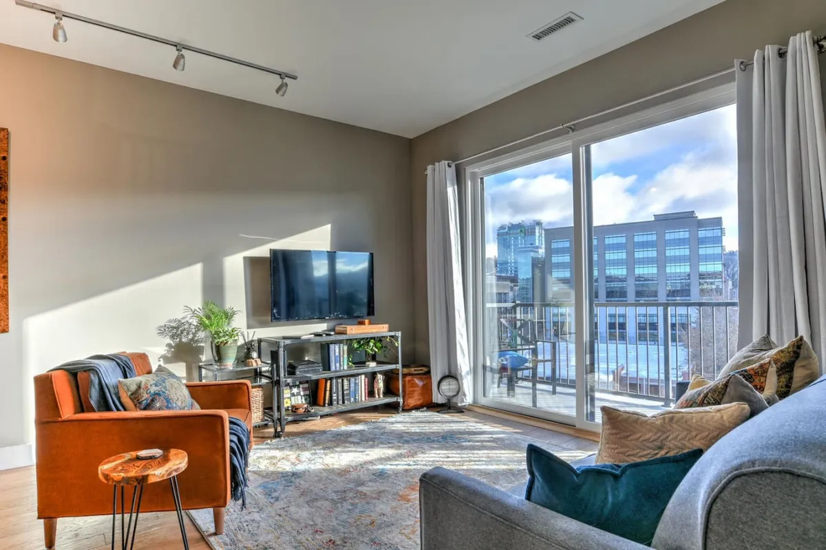 A spacious, cozy living area with large windows offering a direct view of Asheville’s downtown skyline. The comfortable seating area, modern TV, and stylish decor create an inviting scene that highlights both relaxation and the immediate proximity to the city’s attractions.