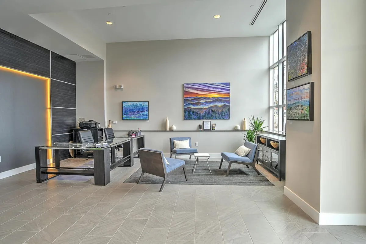 A contemporary interior lobby area with comfortable seating, distinctive artwork on the walls, and a desk area. The space is both welcoming and functional, ideal for arrivals and guest support.